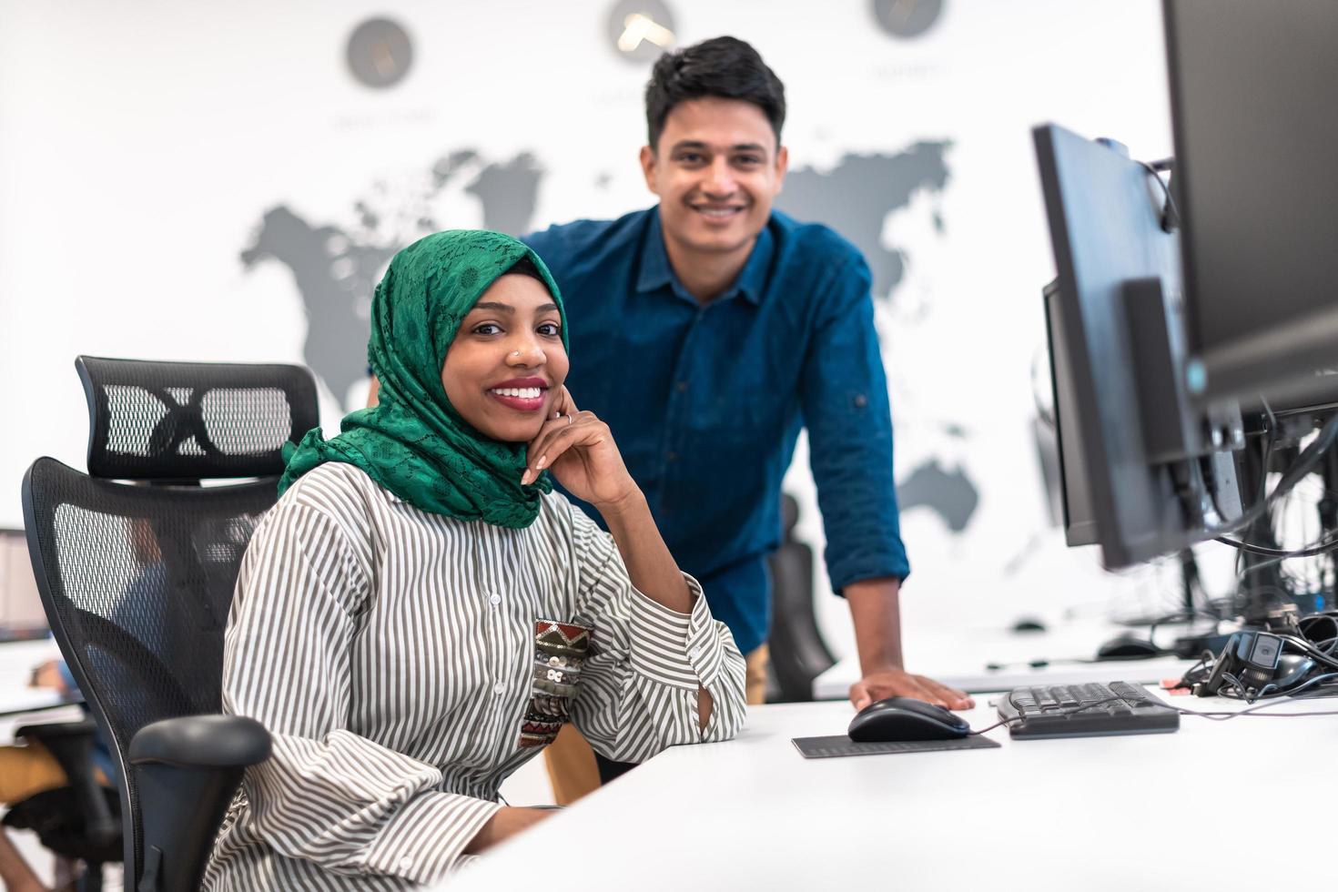 mujer multiétnica del equipo de negocios de inicio que usa un hiyab en una reunión en una moderna oficina de planta abierta con una lluvia de ideas interior, trabajando en una computadora portátil y una computadora de escritorio. enfoque selectivo foto