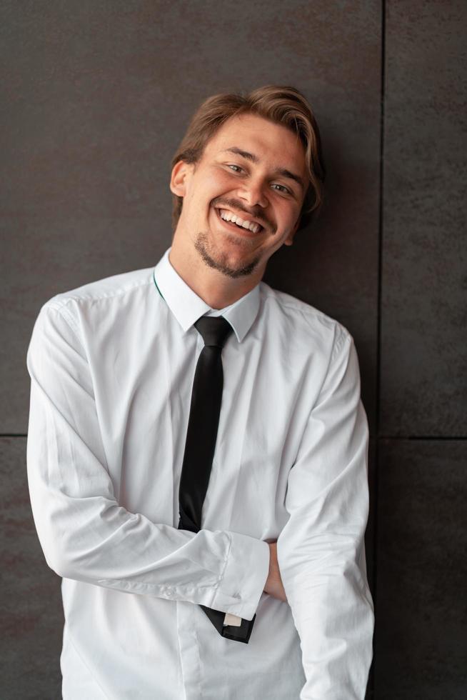 Portrait of startup businessman in a white shirt with a black tie standing in front of gray wall outside photo