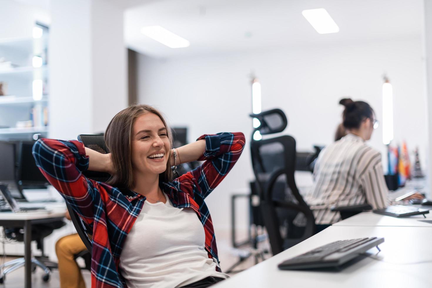 Casual business woman taking a break while working on desktop computer in modern open plan startup office interior. Selective focus photo