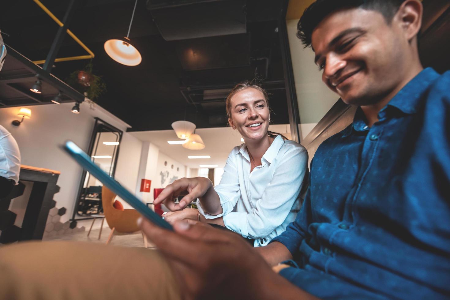 Multiethnic business people man with a female colleague working together on tablet computer in relaxation area of modern startup office photo