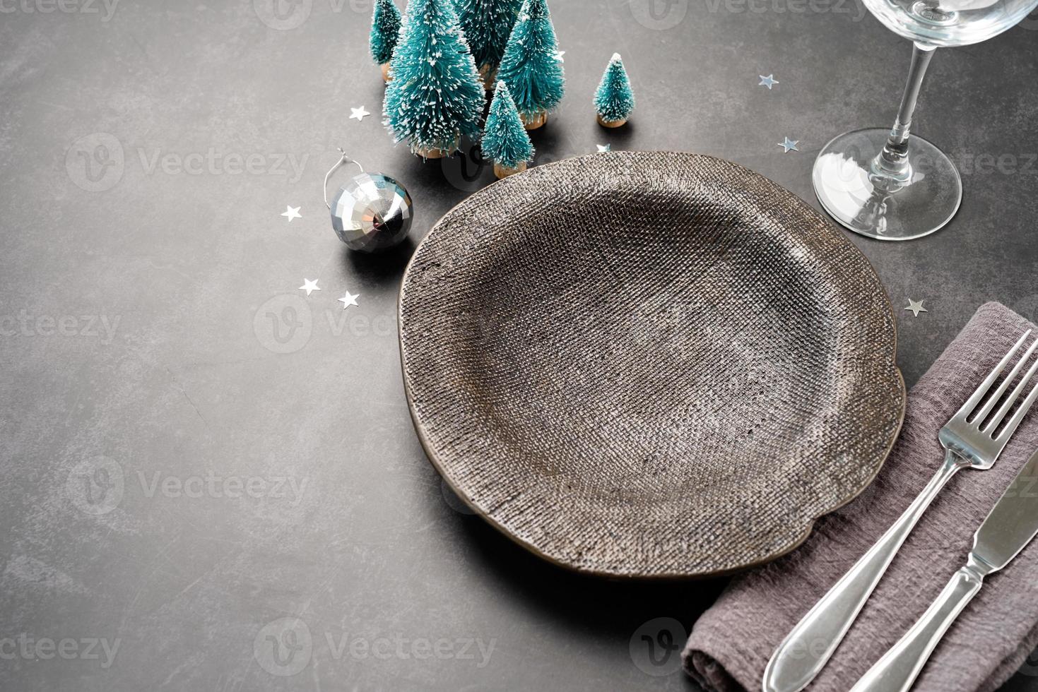 Christmas table setting with black dishware, silverware and green decorations on dark background. Top view. photo