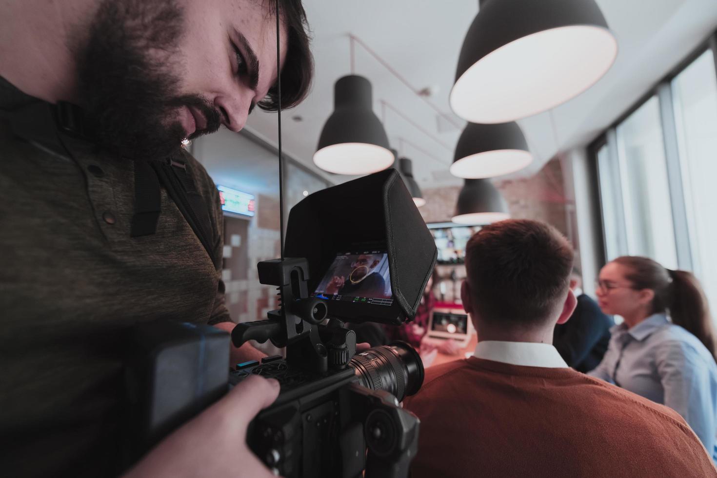 Behind the scene. Cameraman recording a group of young multiethnic business people working and communicating together in a creative office. Selective focus photo