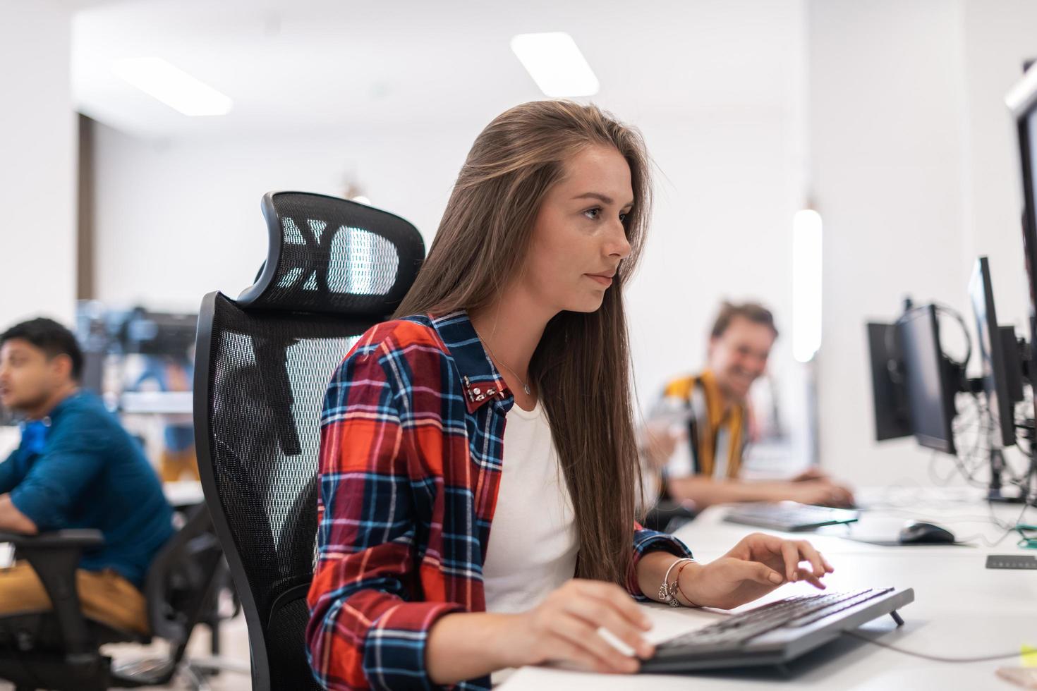 Casual business woman working on desktop computer in modern open plan startup office interior. Selective focus photo