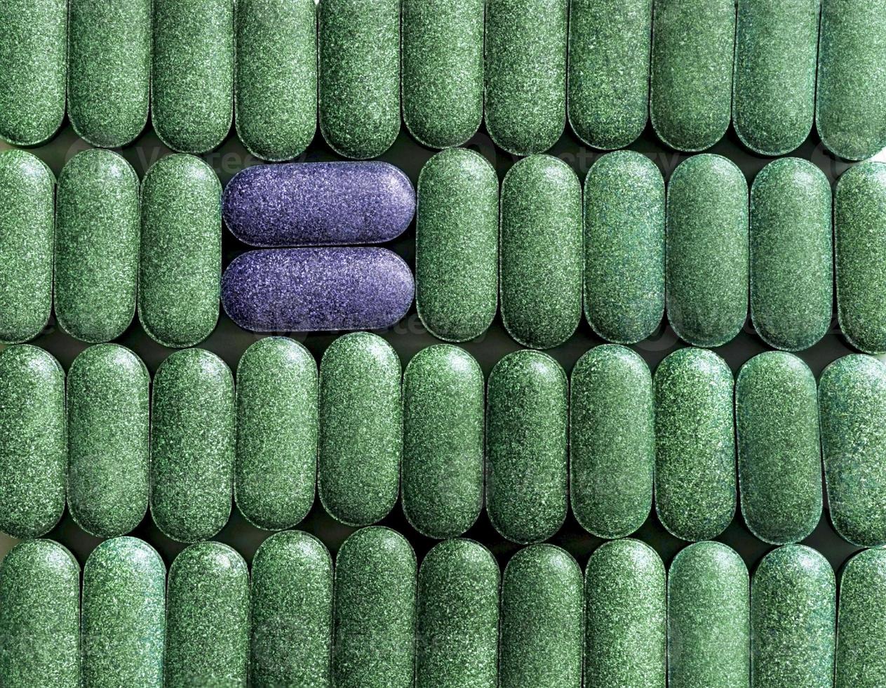 Chlorella, spirulina or barley grass in pill shaped rows and two purple pills across close-up background Nutritional supplement, detox superfood health care photo