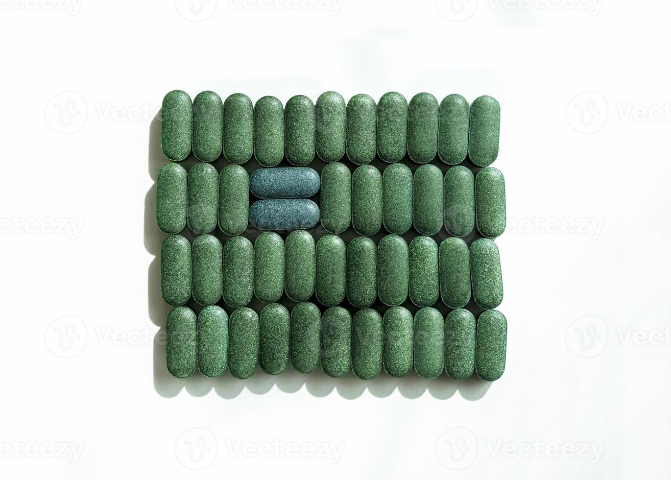 Chlorella, spirulina or barley grass in pill shaped rows and two blue pills across on white background Nutritional supplement, detox superfood health care photo