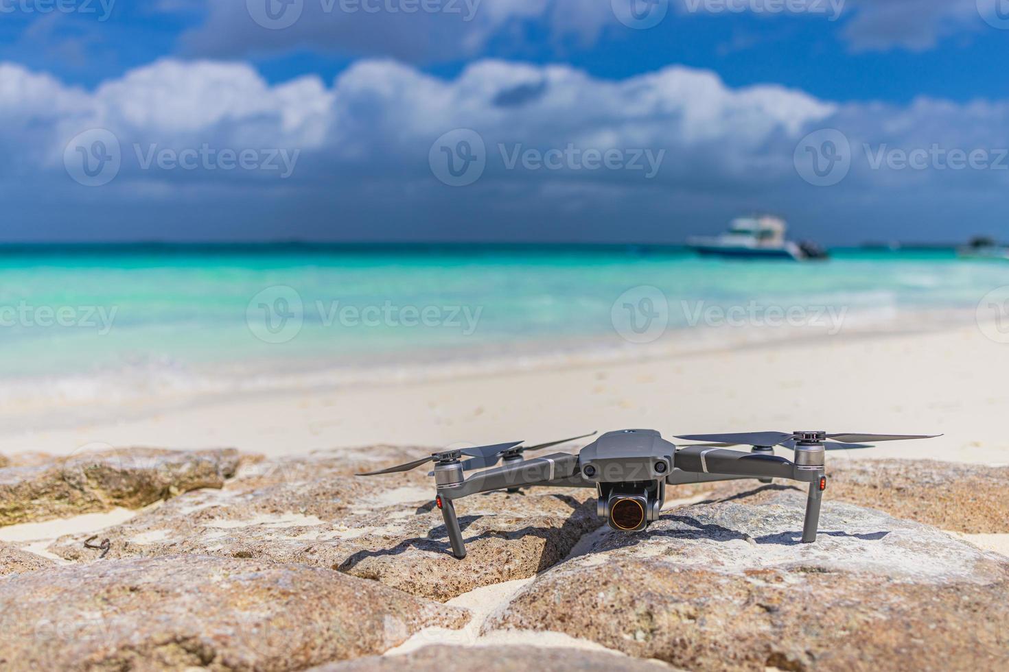 Drone landed on rocks surface next to seashore. Blurred tropical beach shore, coastline landscape, boats and cloudy sky. Luxury filming, footage and content creating for tourism, advertising photo