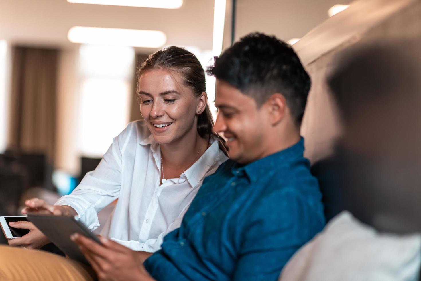 Multiethnic business people man with a female colleague working together on tablet computer in relaxation area of modern startup office photo