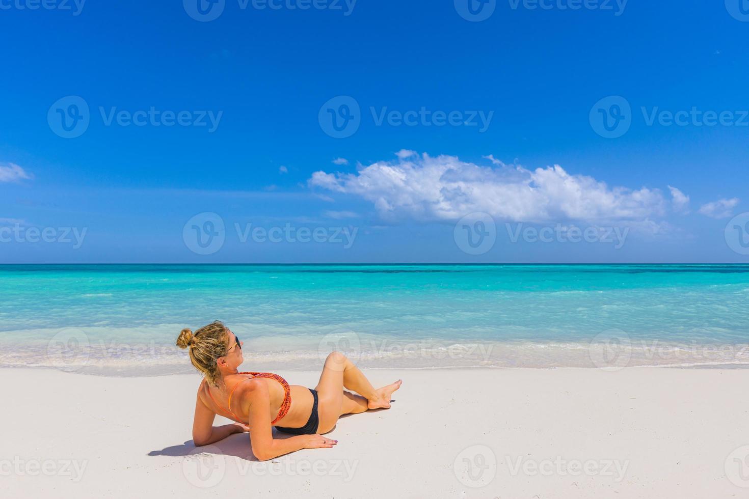 Woman relaxing on the beach. Sexy bikini body legs, sunglasses woman enjoying paradise tropical beach. Exotic shore, sea water as freedom concept. Beautiful carefree fit body girl on travel vacation photo