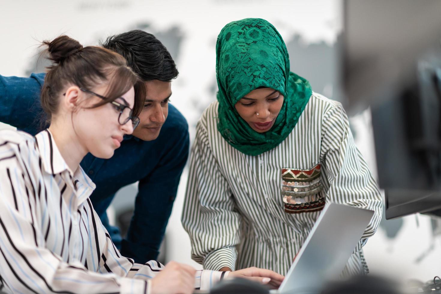 Multiethnic startup business team Arabian woman wearing a hijab on meeting in modern open plan office interior brainstorming, working on laptop and desktop computer. Selective focus photo