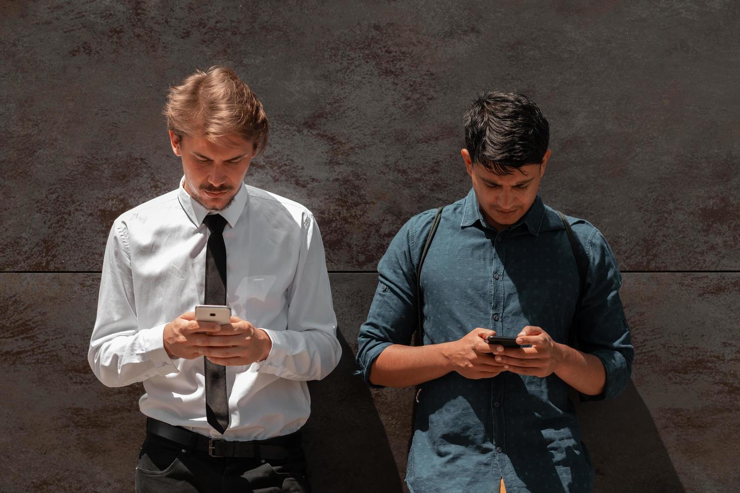 Casual multiethnic startup business men one of them is Indian using smartphone during break from work in front of grey wall outside photo