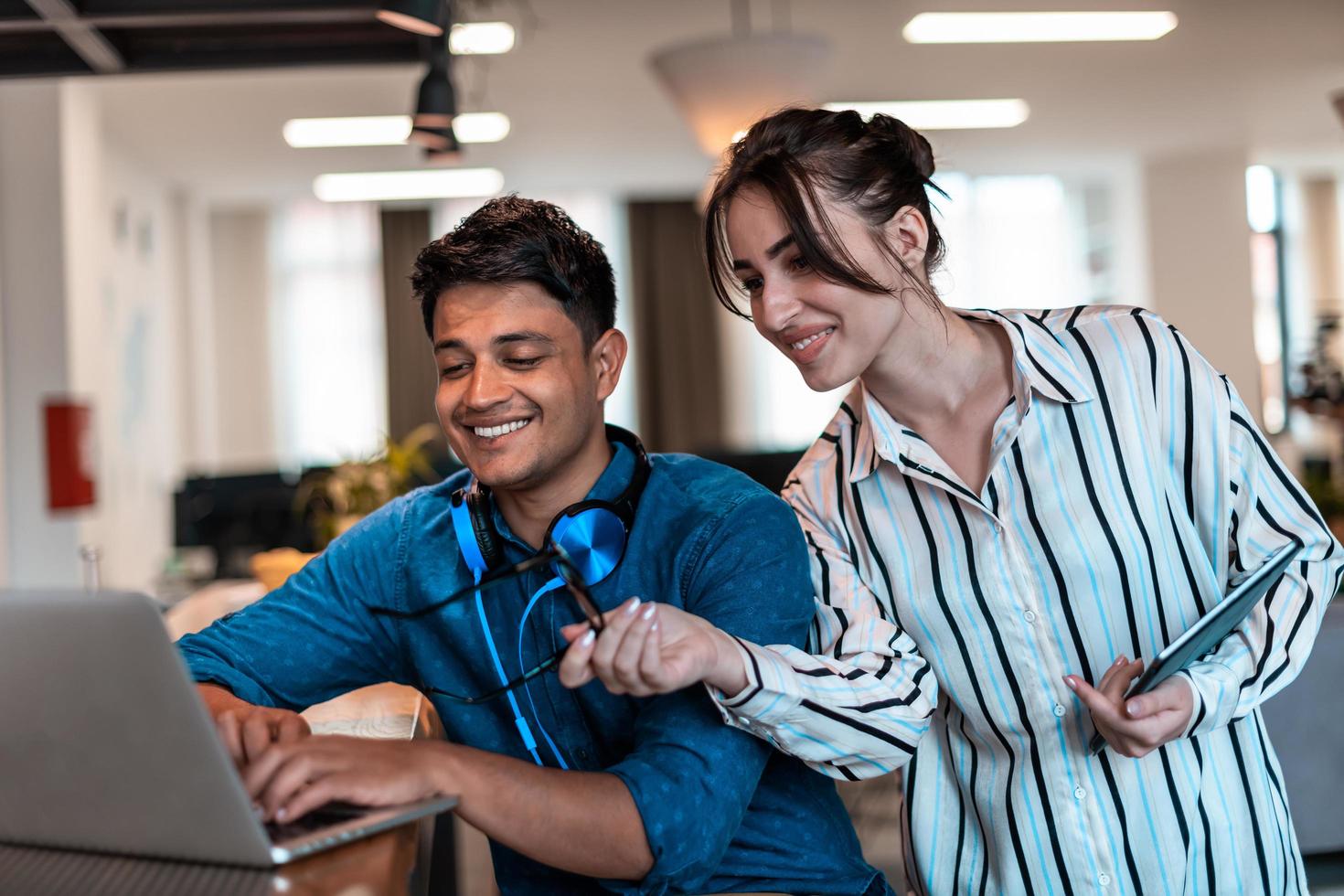 Multiethnic business people man with a female colleague working together on tablet and laptop computer in relaxation area of modern startup office photo