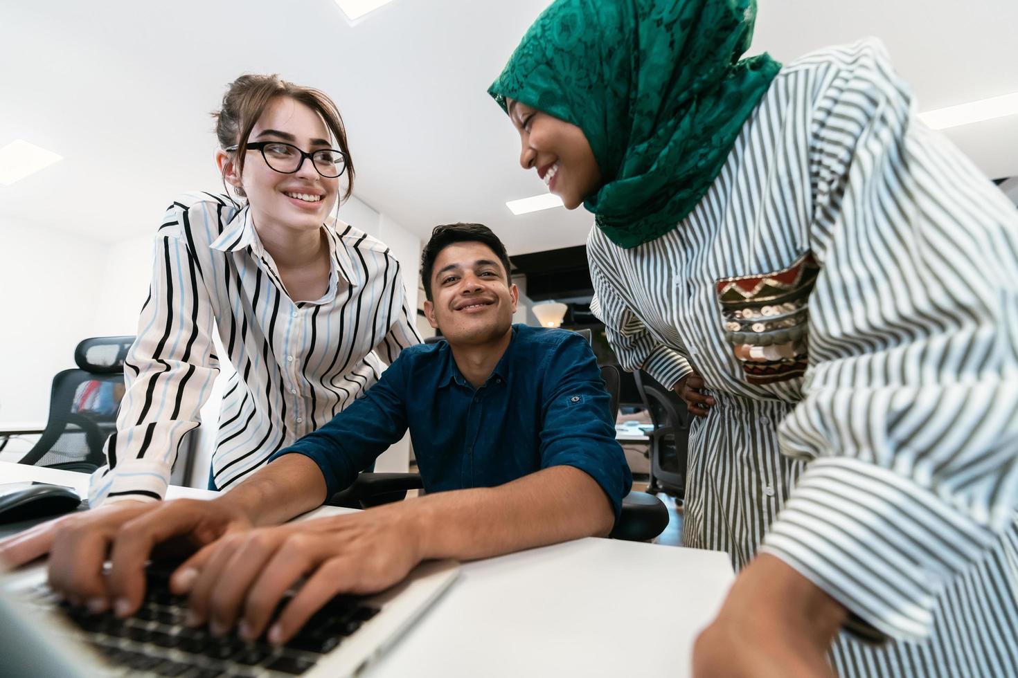 Multiethnic startup business team Arabian woman wearing a hijab on meeting in modern open plan office interior brainstorming, working on laptop and desktop computer. Selective focus photo