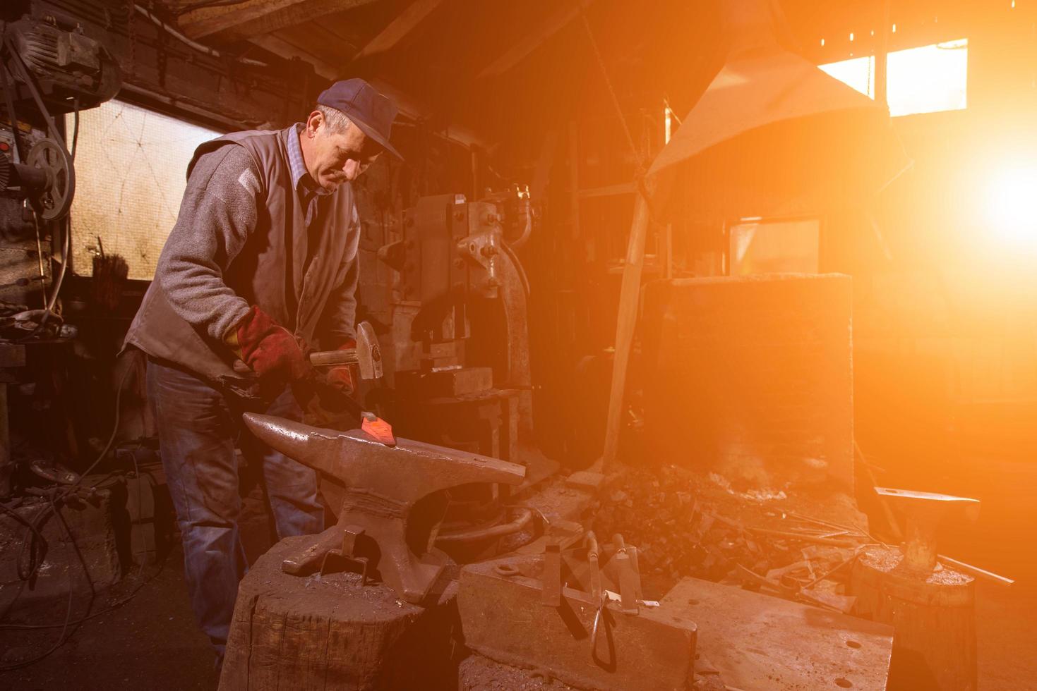 blacksmith manually forging the molten metal with sunlight through the windows photo