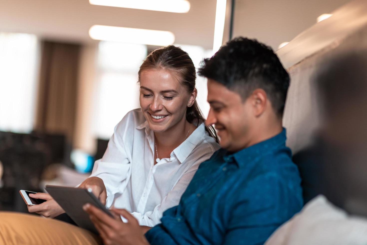 Multiethnic business people man with a female colleague working together on tablet computer in relaxation area of modern startup office photo