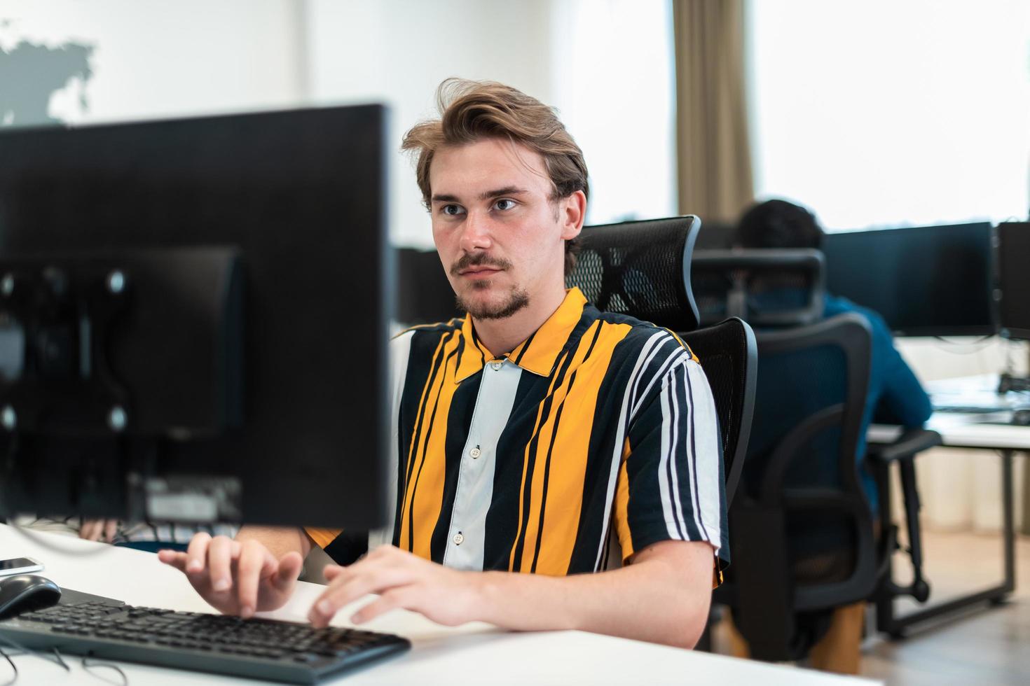 Casual man working on desktop computer in modern open plan startup office interior. Selective focus photo