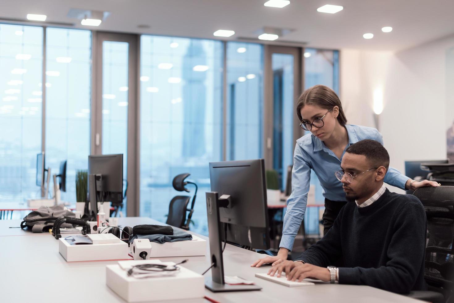 Young smiling woman explaining to serious African American coworker project strategy. Diverse startup coworkers students woman and man talking discussing working in modern office using computer. photo