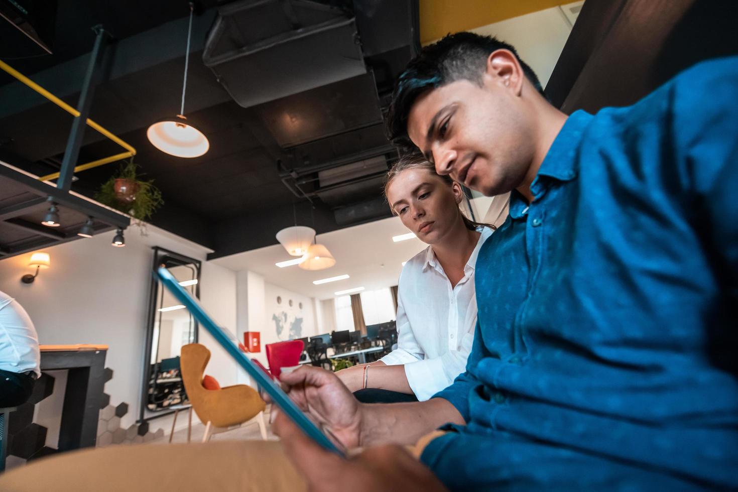 Multiethnic business people man with a female colleague working together on tablet computer in relaxation area of modern startup office photo