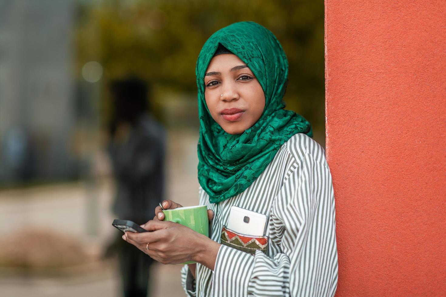 African Muslim businesswoman with green hijab using mobile phone during coffee break from work outside photo