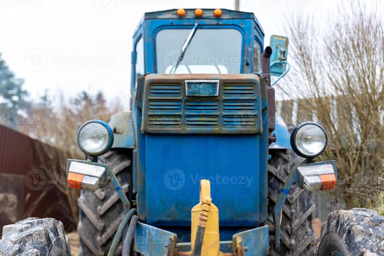 old blue tractor front photo with fence and trees on background