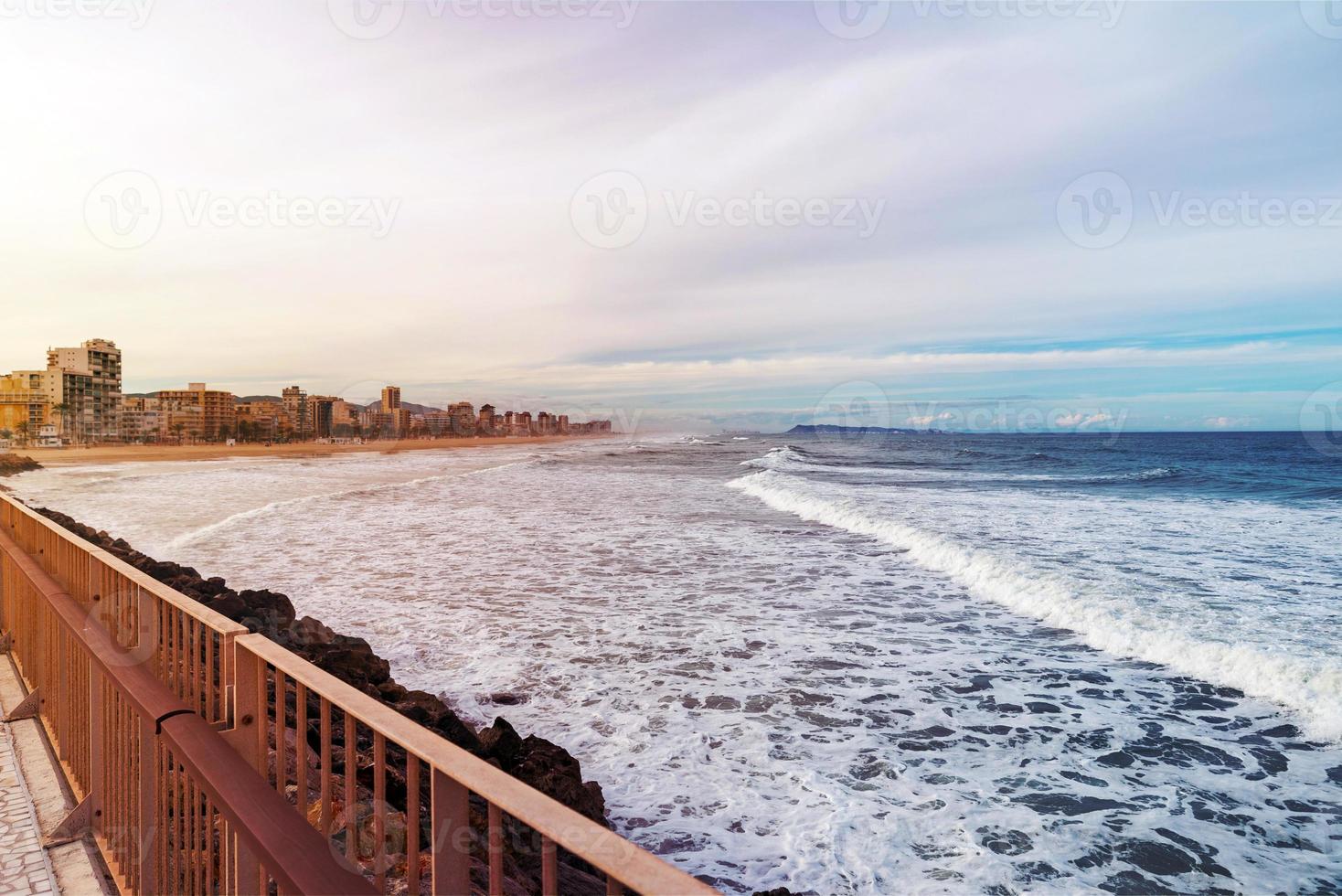 view of the coastal city and sea waves with a breakwater and a mountain in the clouds in the background photo