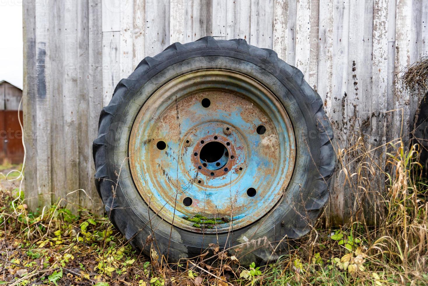 una gran rueda azul oxidada de un tractor se encuentra cerca de la pared del granero foto