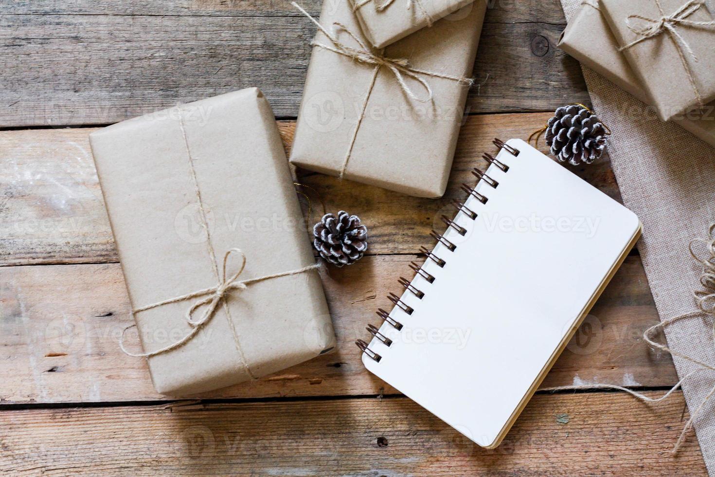 caja de regalo de navidad use papel reciclado marrón y un cuaderno y piñas en una mesa de madera. foto