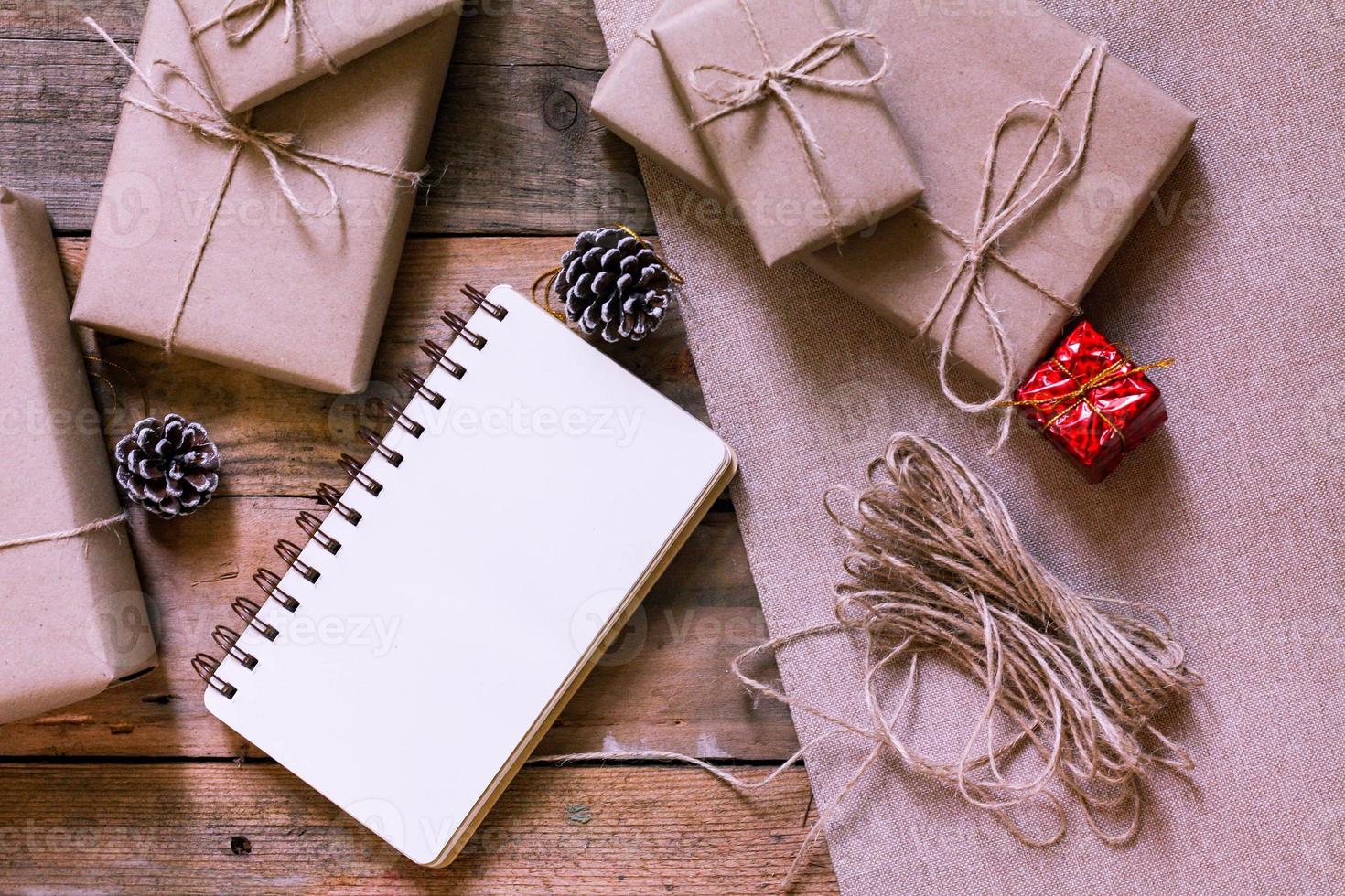 caja de regalo de navidad use papel reciclado marrón y un cuaderno y piñas en una mesa de madera. foto