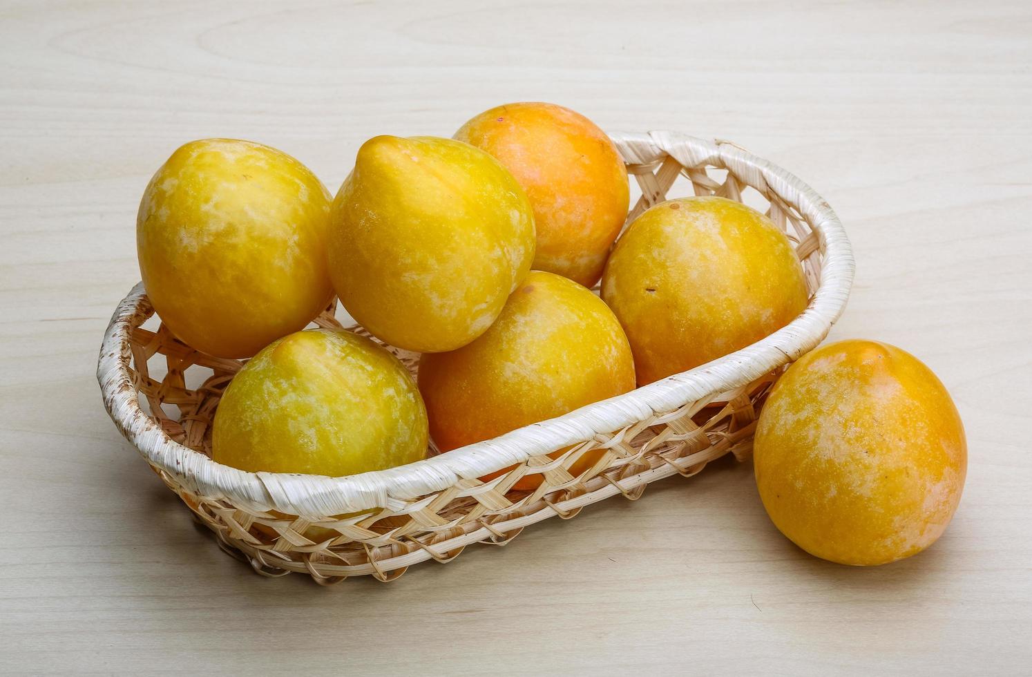 Yellow plums in a basket on wooden background photo