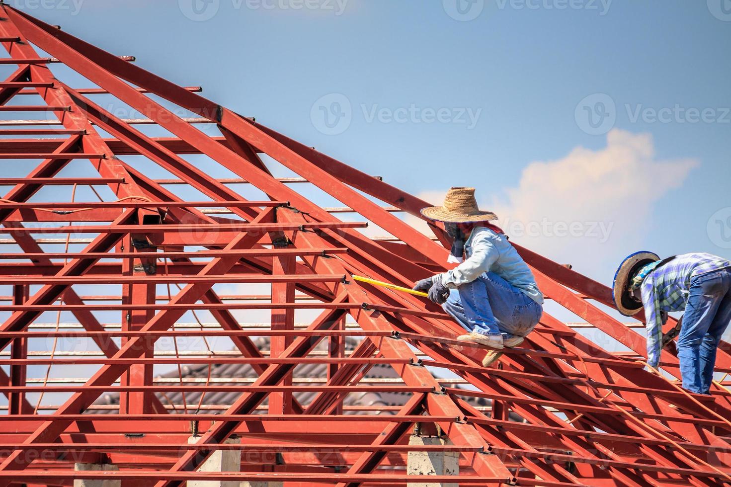 welder workers installing steel frame structure of the house roof at building construction site photo