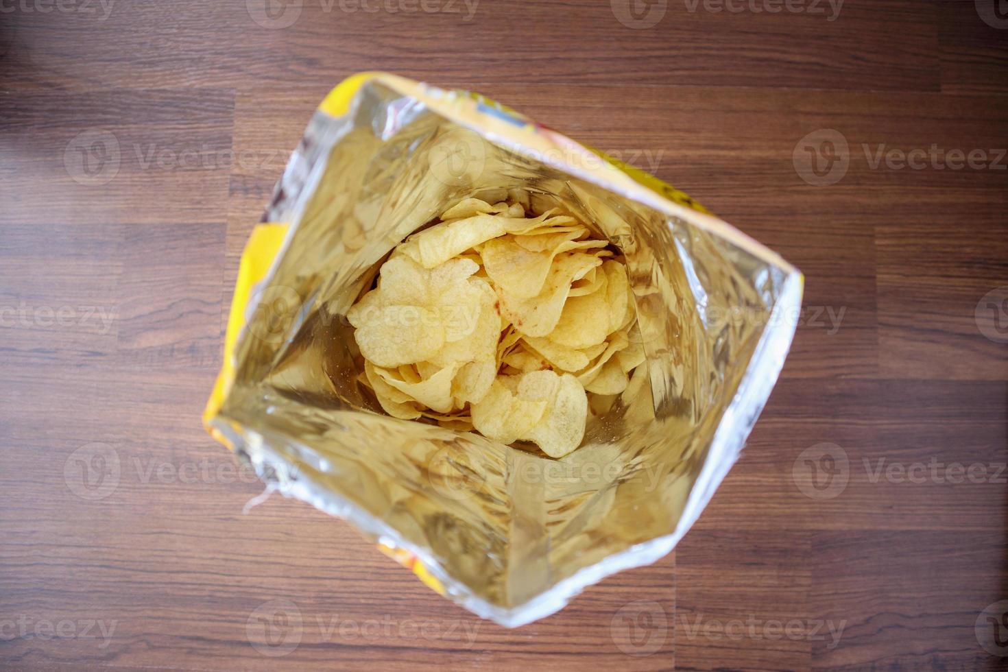 Potato chips in open snack bag close up on table floor photo