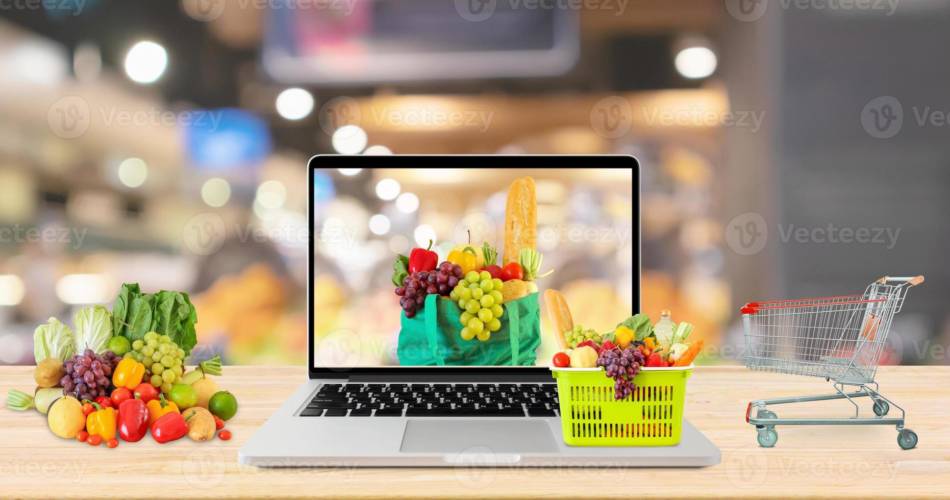 supermarket aisle blurred background with laptop computer and shopping cart on wood table grocery online concept photo