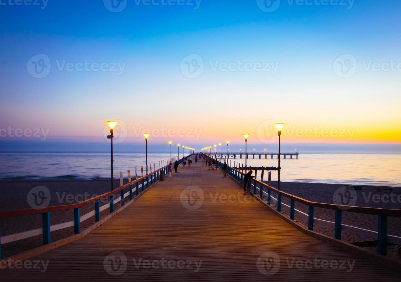 Illuminated romantic vintage Palanga pier after sunset with people walking in beautiful summer evening. Lithuania summer holiday landmarks destination photo