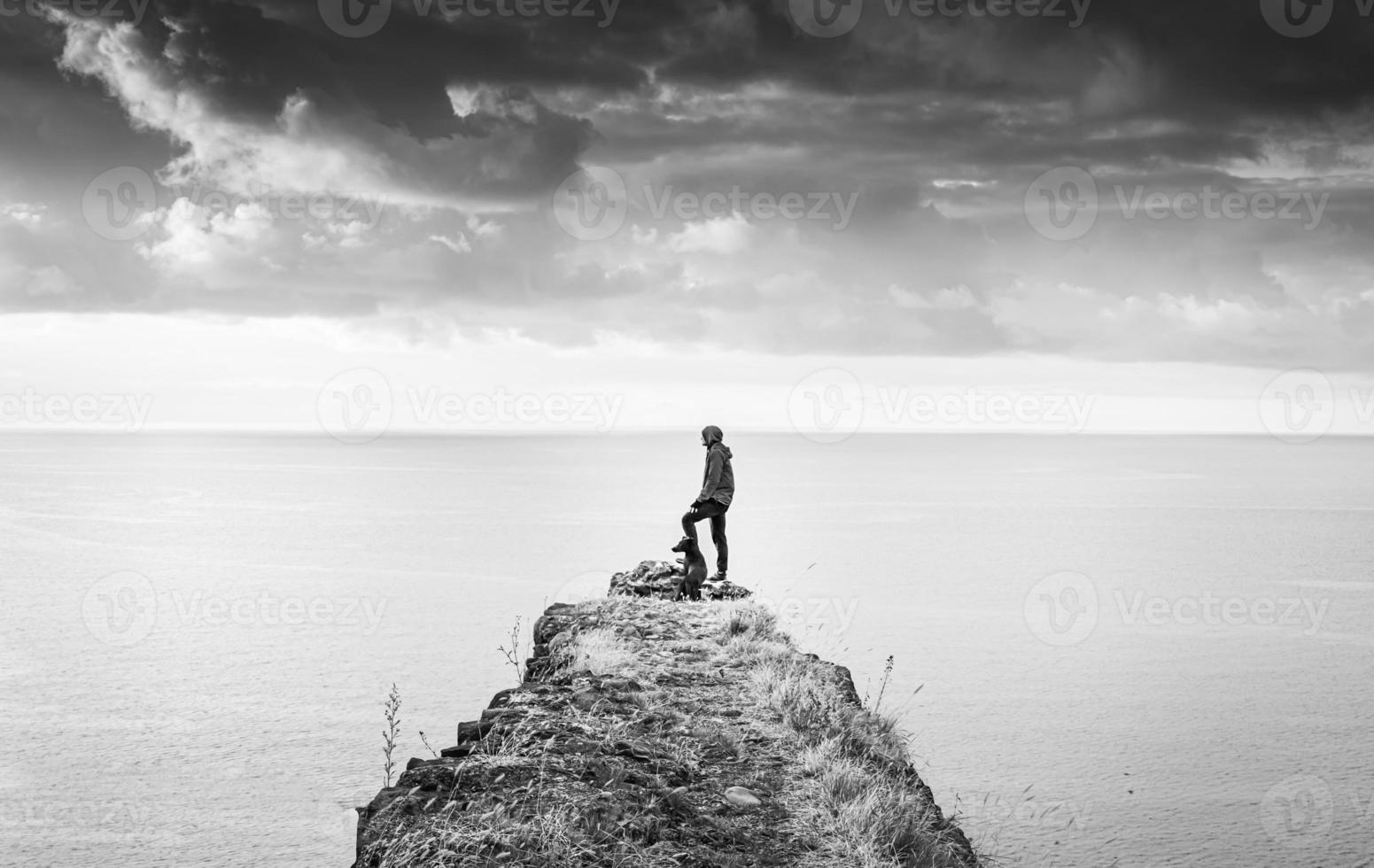 el propósito de la búsqueda de la persona masculina en la vida se encuentra perdido en el borde del acantilado con su amigo perro y mira a la izquierda el vasto paisaje marino. concepto de amistad y paz foto