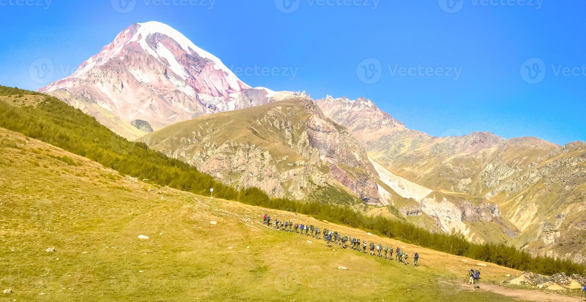 Guided group of mountaineers hiking up the hill with KAzbek mountain peak in the background. Kazbeki national park. photo