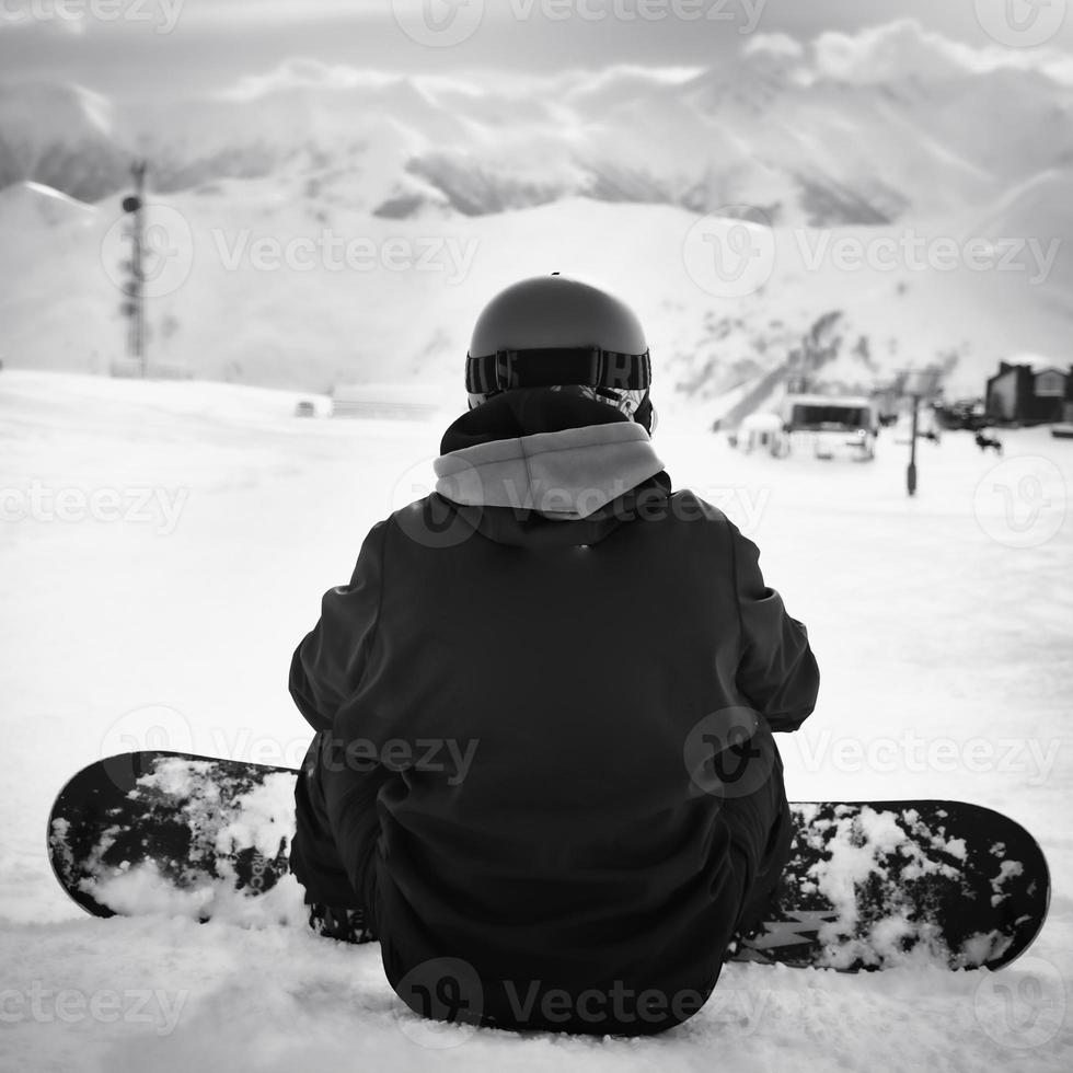 Male man snowboarder sit enjoy inter mountain panorama in ski resort alone in majestic mountains. photo