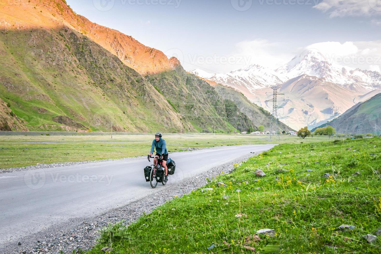 ciclista varón caucásico en bicicleta en las montañas kazbegi del cáucaso y el pico kazbek en el fondo. viajar por el cáucaso. ciclo alrededor del mundo foto