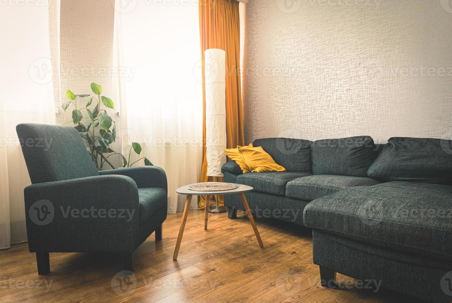 Cozy apartment living room with sofa and yellow pillows and stylisg table with book by flower and window with blue light outside in winter. Grey armchair .opy paste wall background photo