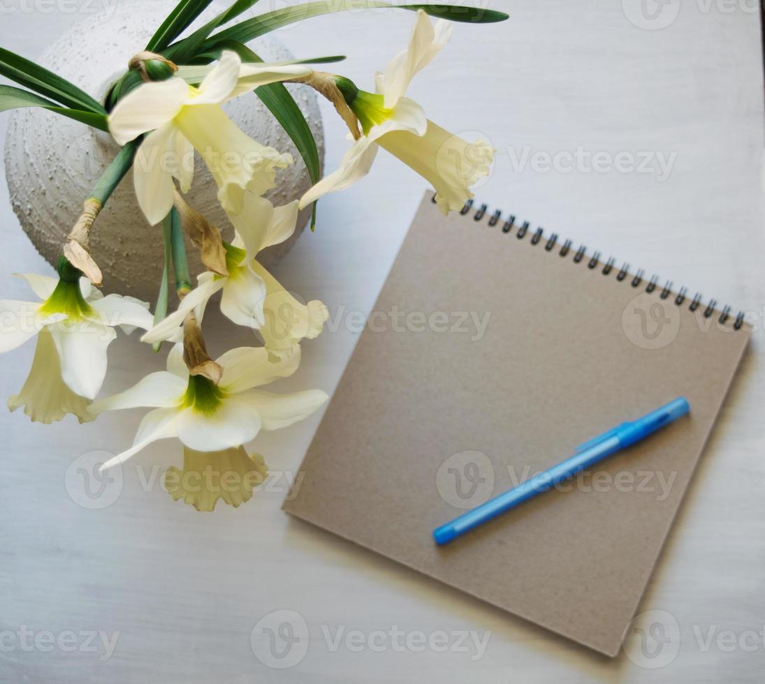 Notepad with pen, daffodils in a vase on a white table. Inspirational workplace. photo