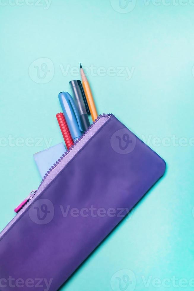Fashionable violet pencil case with multicolored felt-tip pens, pencils and pens on green background. photo