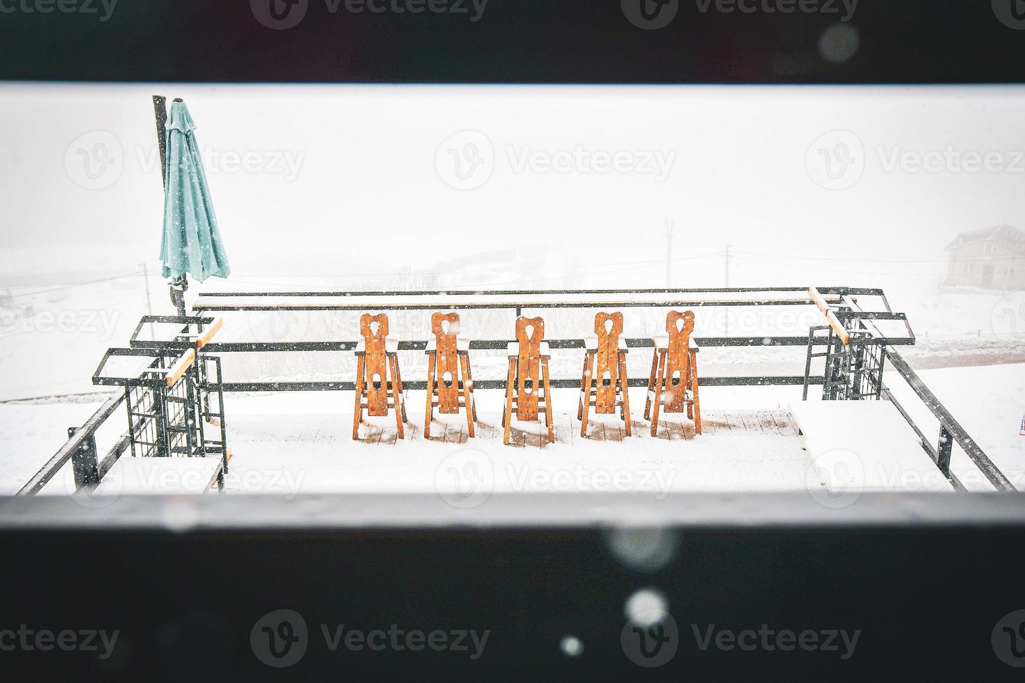 Chairs on snow in snowy day in ski resort restaurant. Bad weather fresh snow in winter holiday resort. photo