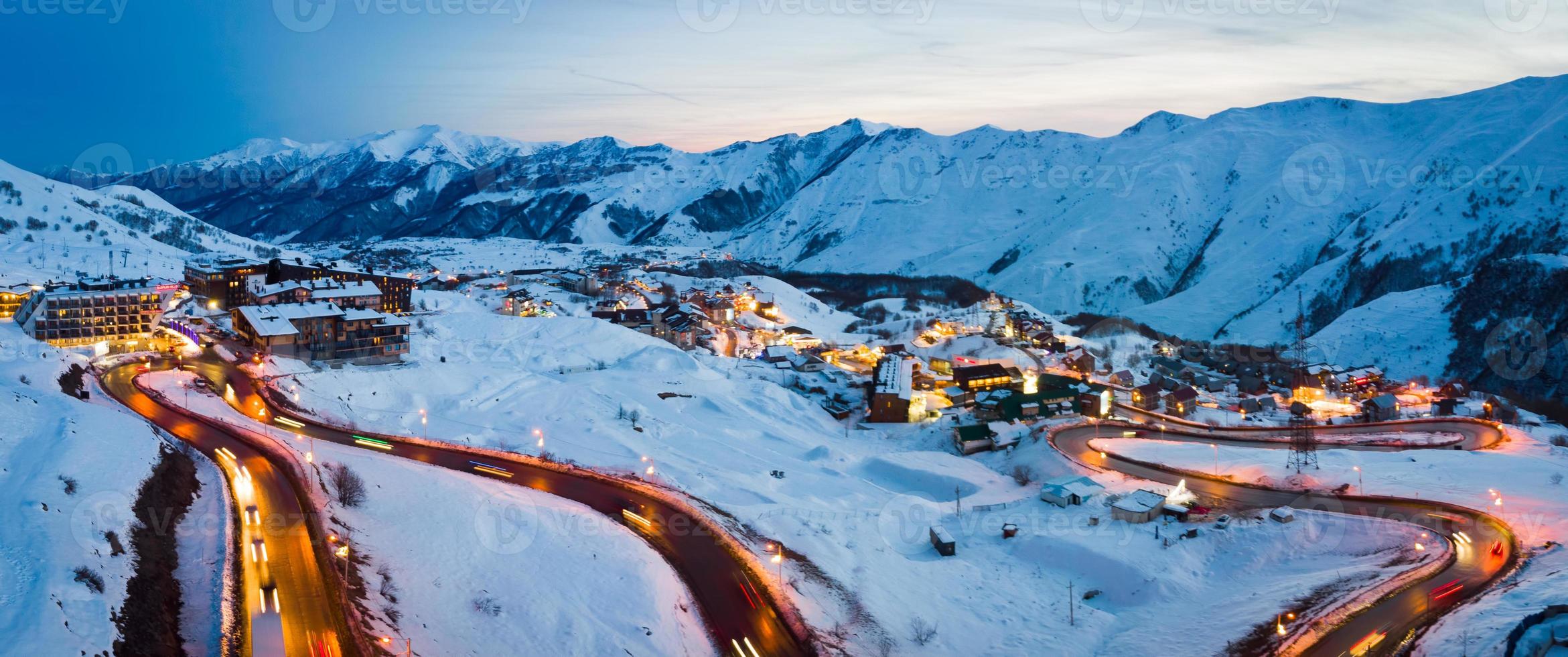 Scenic winter landscape in Gudauri with caucasus mountains background and holiday hotels and road with cars on evening photo