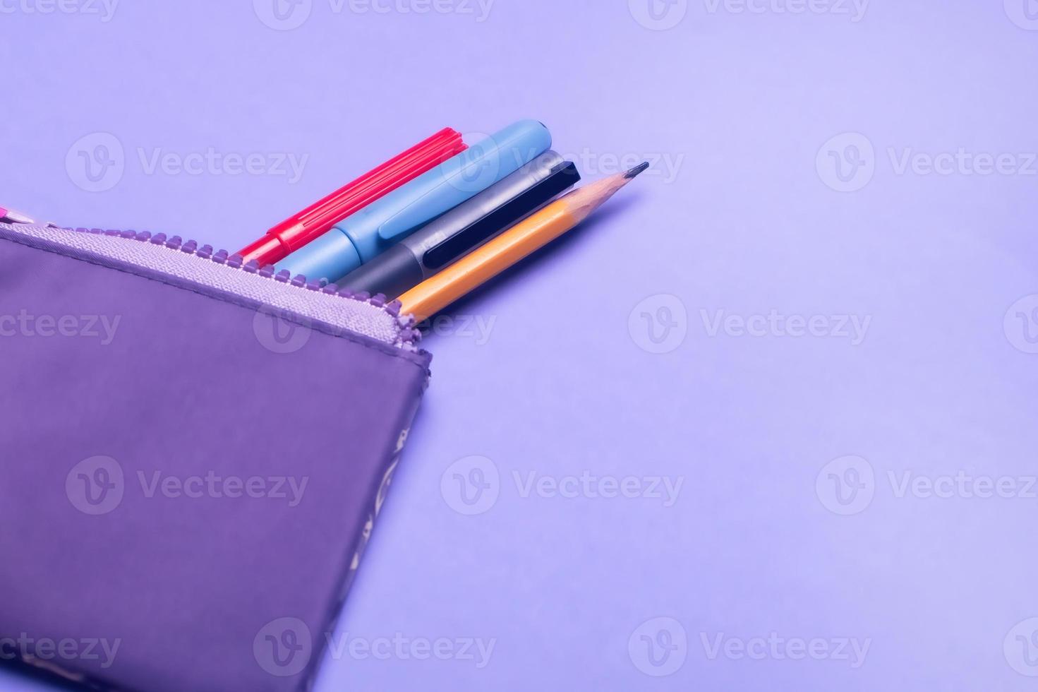 Fashionable violet pencil case with multicolored felt-tip pens, pencils and pens on lilac background. photo