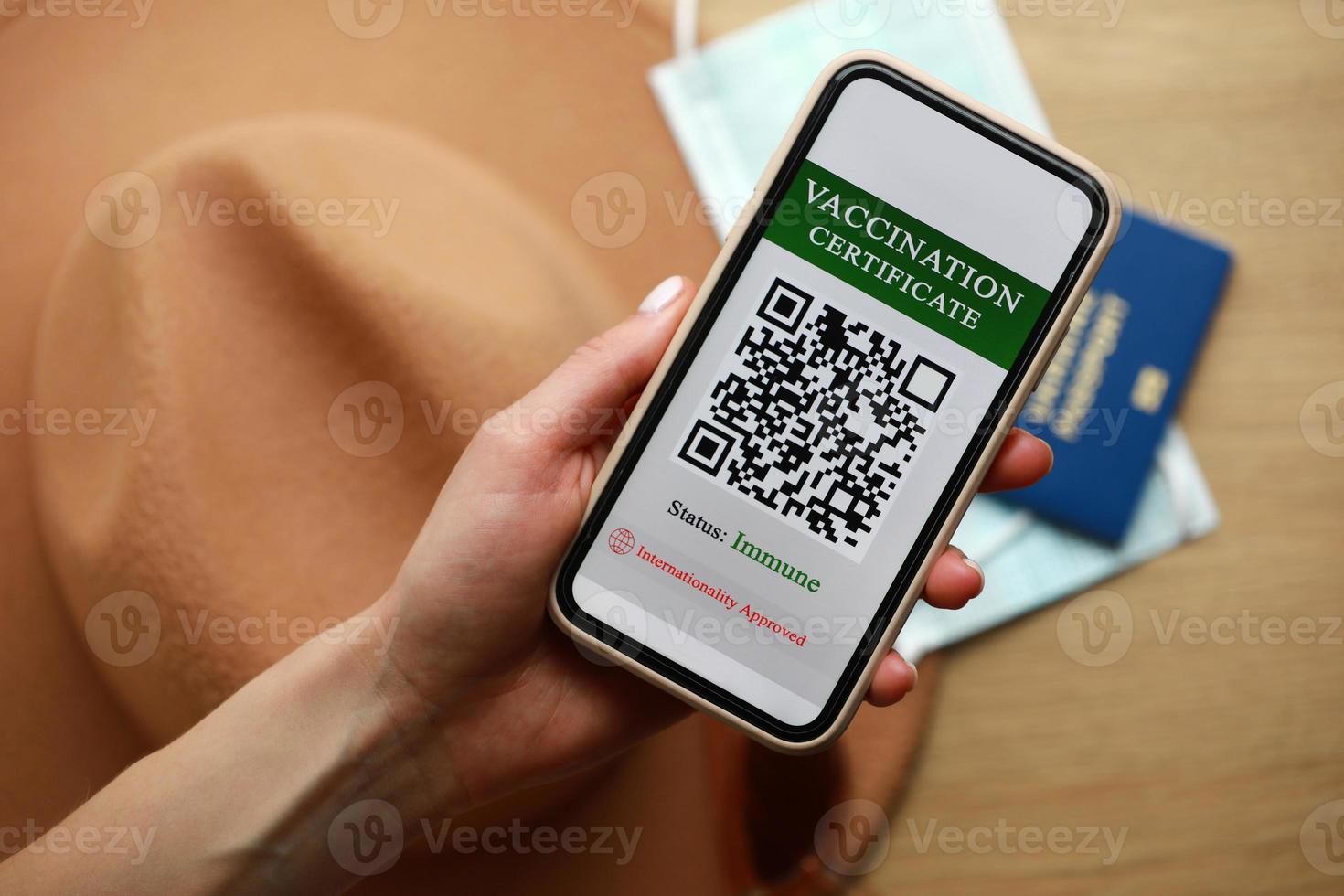 New normal concept. Close up view of female's hold a smartphone with an immune digital health passport. In the background, a sunglasses, protective mask, hat and passport. in a blur. photo