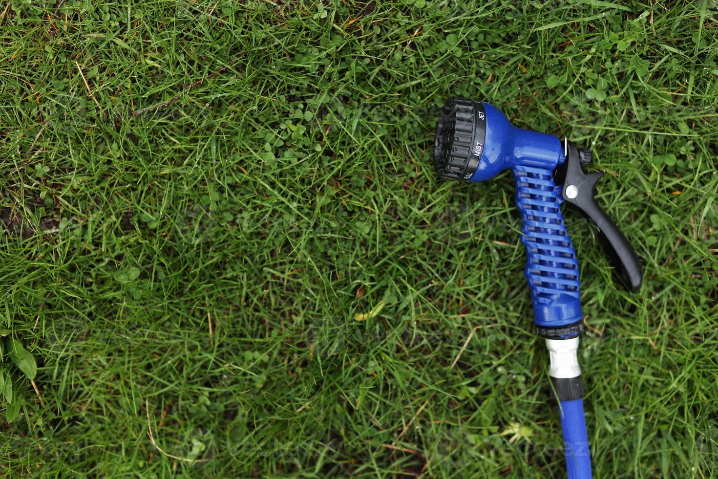 Blue gun spray water on the hose for watering the lawn. Blue spray gun for watering green grass. Irrigation of the garden with a garden hose. Gardening. Farming. Agriculture. Place for your text photo
