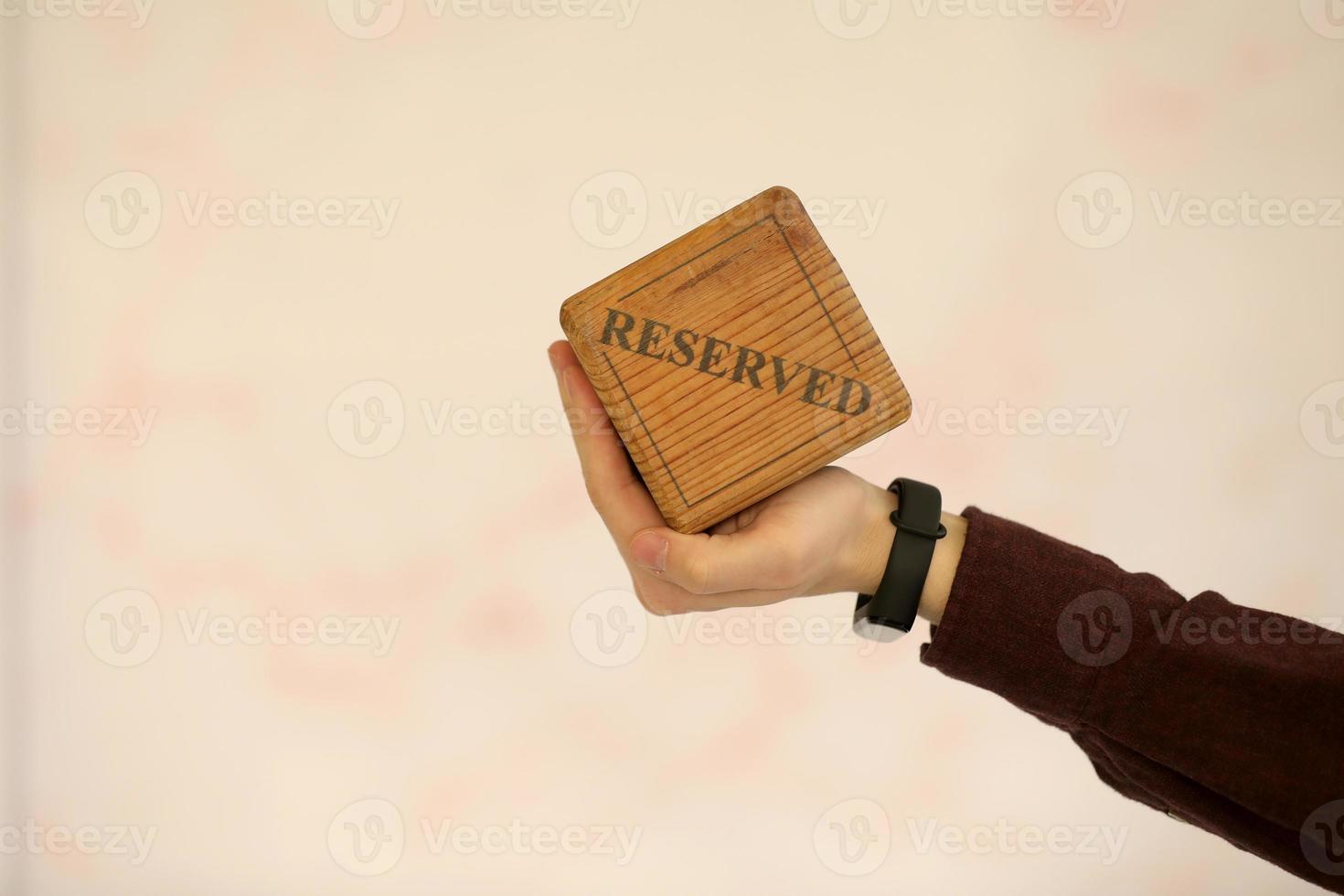 A wooden plaque has a word reserved . male hand holds a wooden plate with the inscription reserved isolated on a white background. selective focus photo