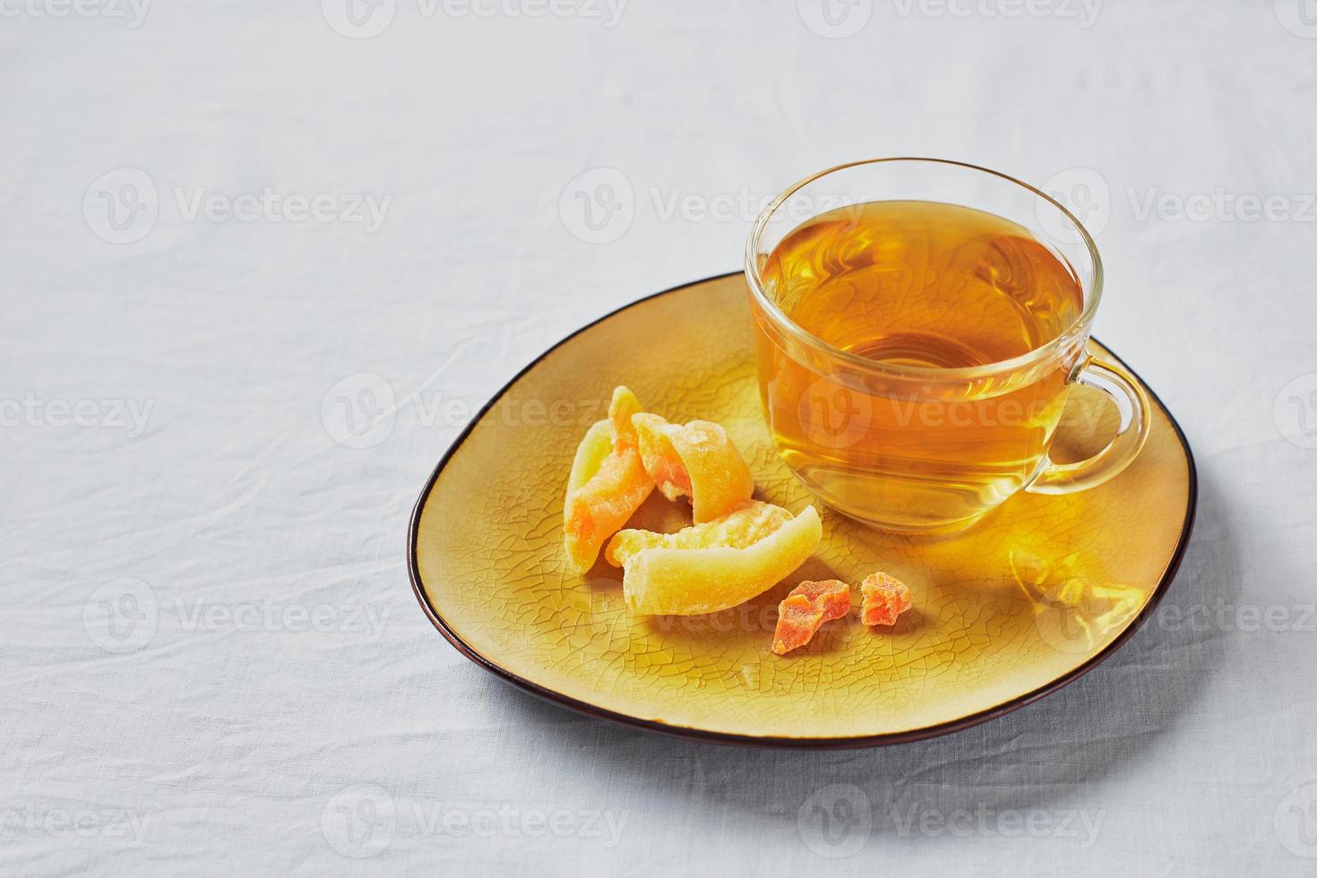 Delicious black tea in glass cup and candied fruits on yellow saucer