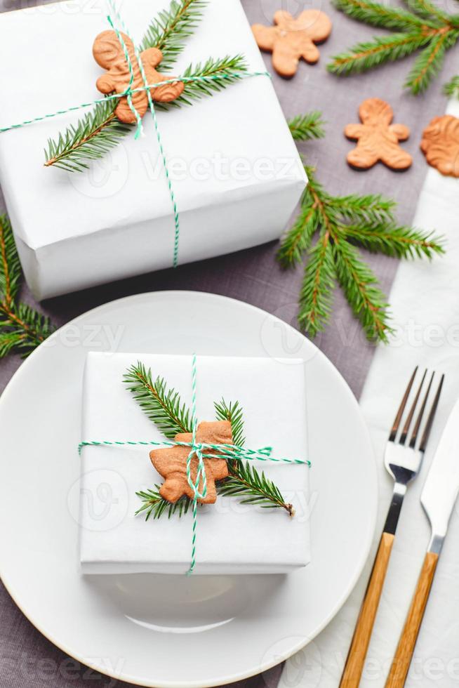 Christmas festive table setting, plate with gift decorated with spruce sprigs and gingerbread photo