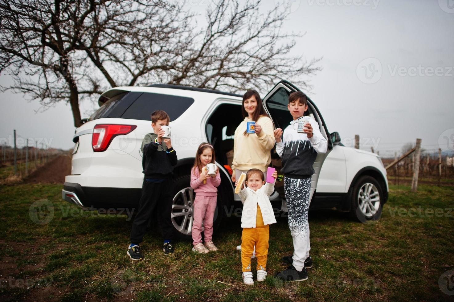 Mother with kids drink tea outdoor near white suv car. photo