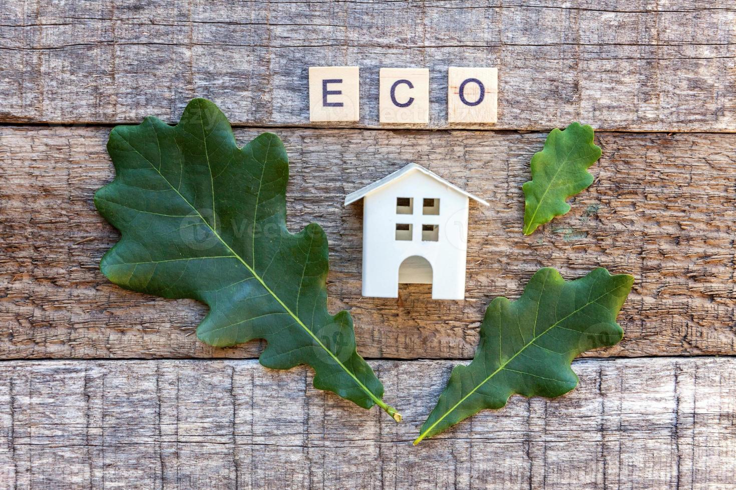 Miniature toy model house with inscription ECO letters word on wooden background photo