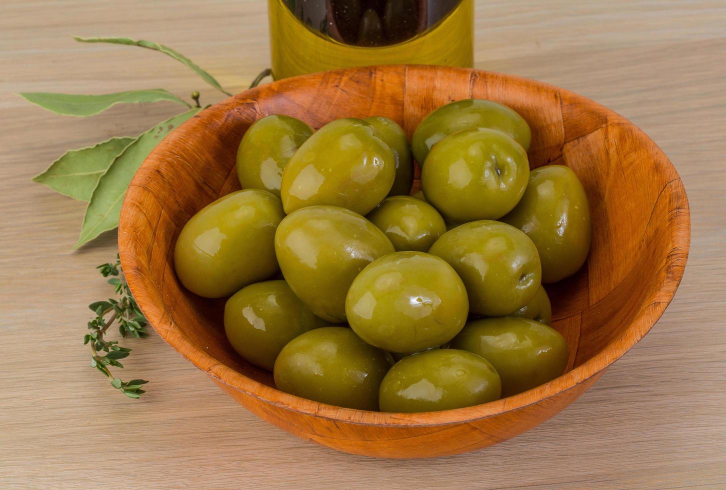 aceitunas verdes en un recipiente sobre fondo de madera foto